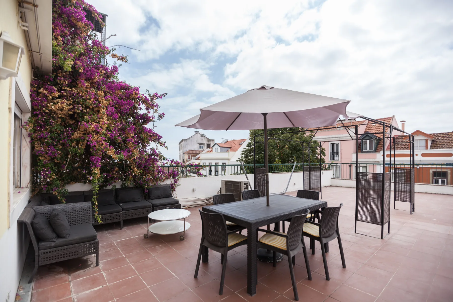 Terraza amueblada con asientos al aire libre, una mesa de comedor y una sombrilla grande.