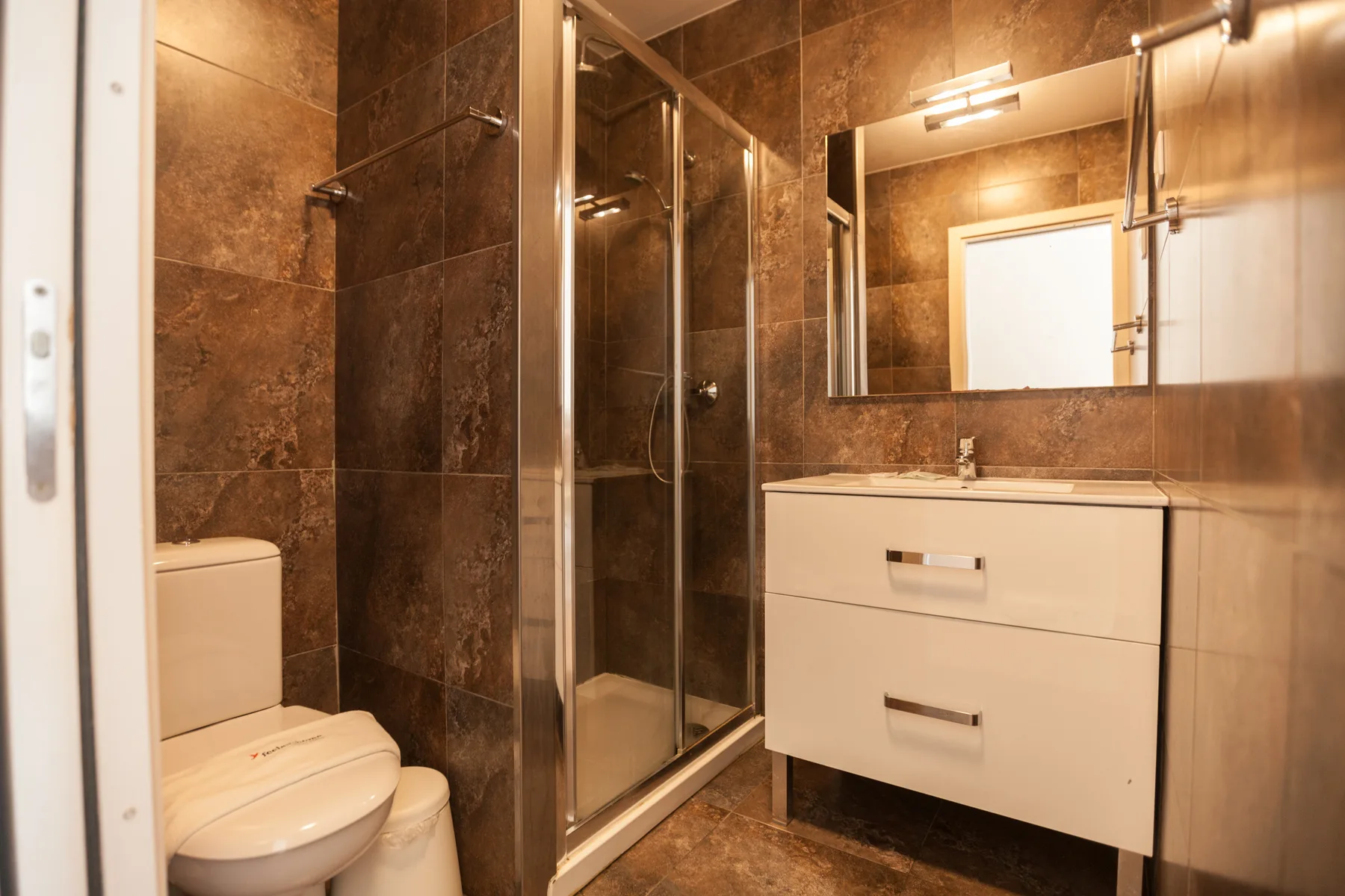 Un baño alicatado con ducha, inodoro y mueble de lavabo.