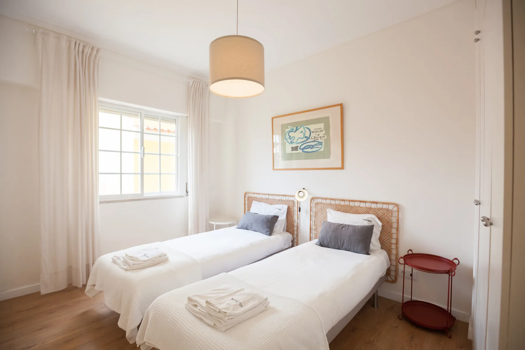 Dormitorio luminoso con dos camas individuales, una ventana y un cuadro en la pared.