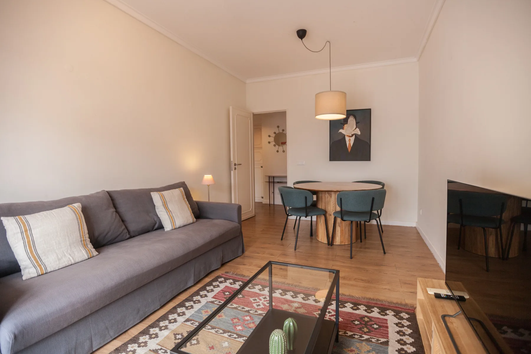 Una sala de estar con sofá gris, alfombra estampada y mesa de comedor.