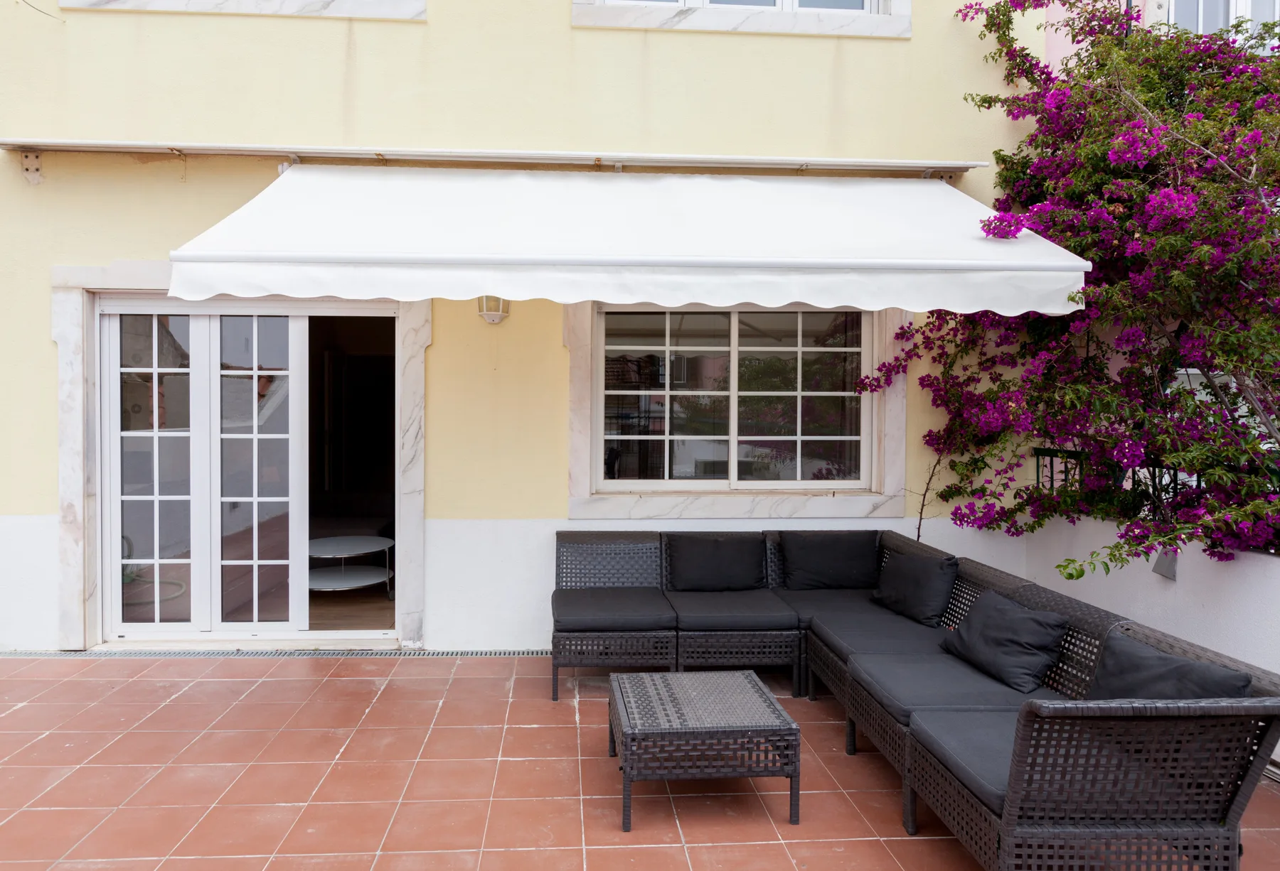 Un patio embaldosado tiene asientos oscuros al aire libre bajo un toldo blanco.