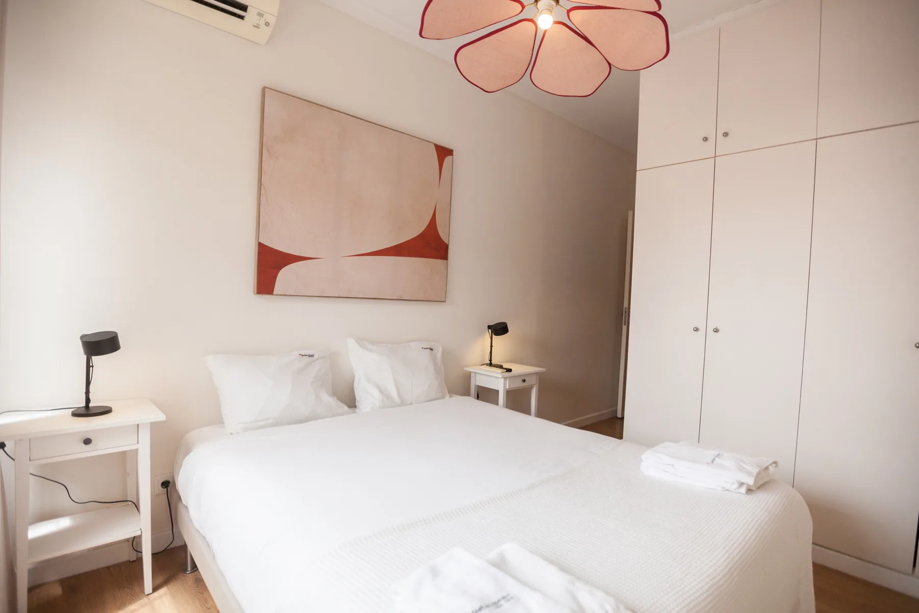 Un dormitorio luminoso con ropa de cama blanca, mesitas de noche y arte abstracto en la pared.