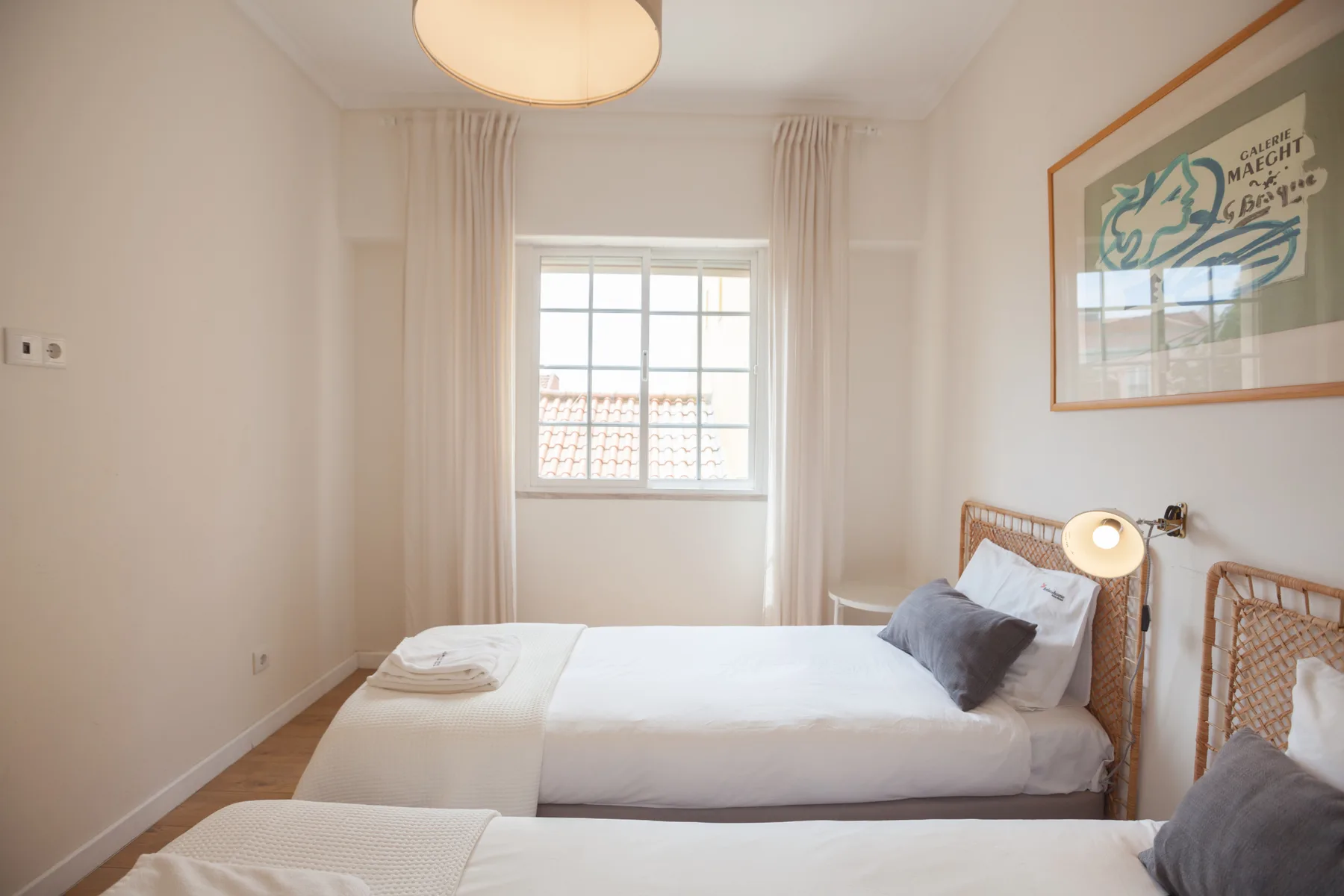 Un dormitorio luminoso con ropa de cama blanca, una ventana y una lámina enmarcada.