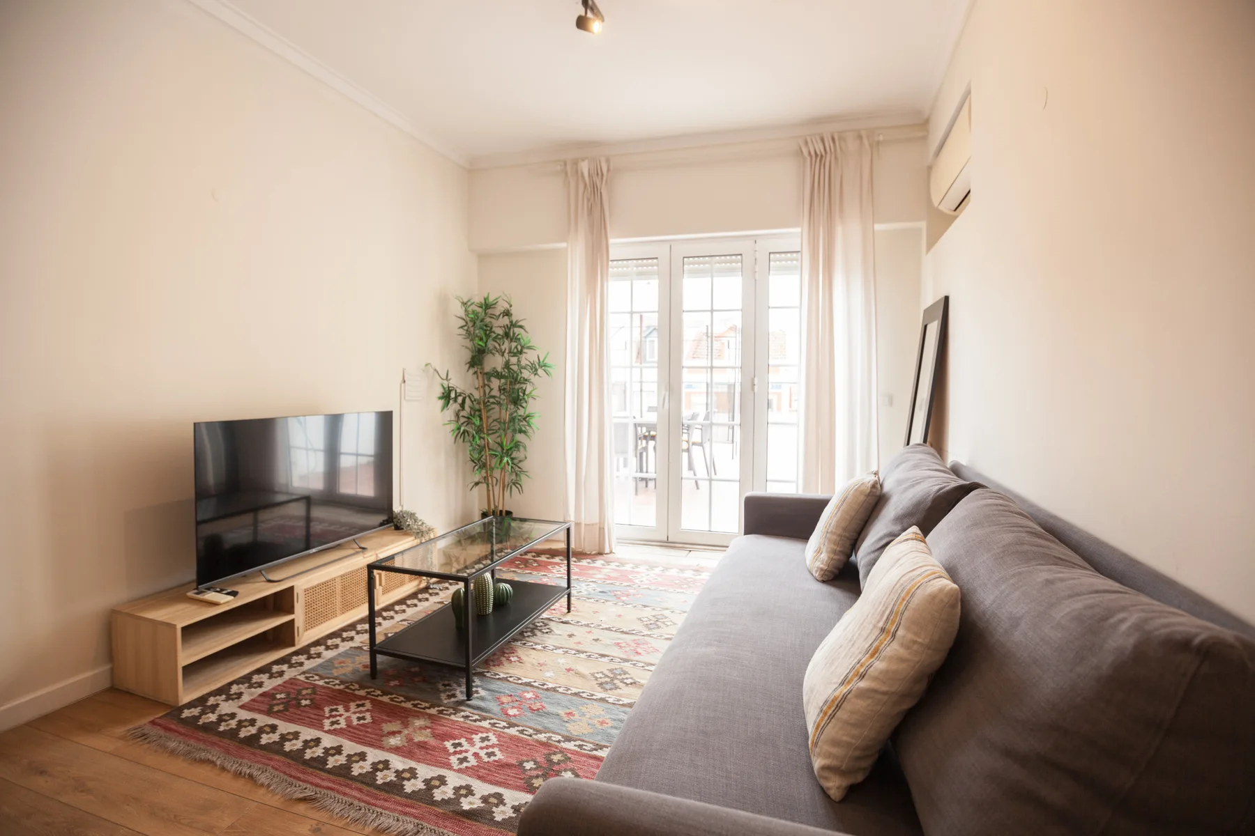 Una sala luminosa con asientos, un televisor y ventanales que dan a un balcón.