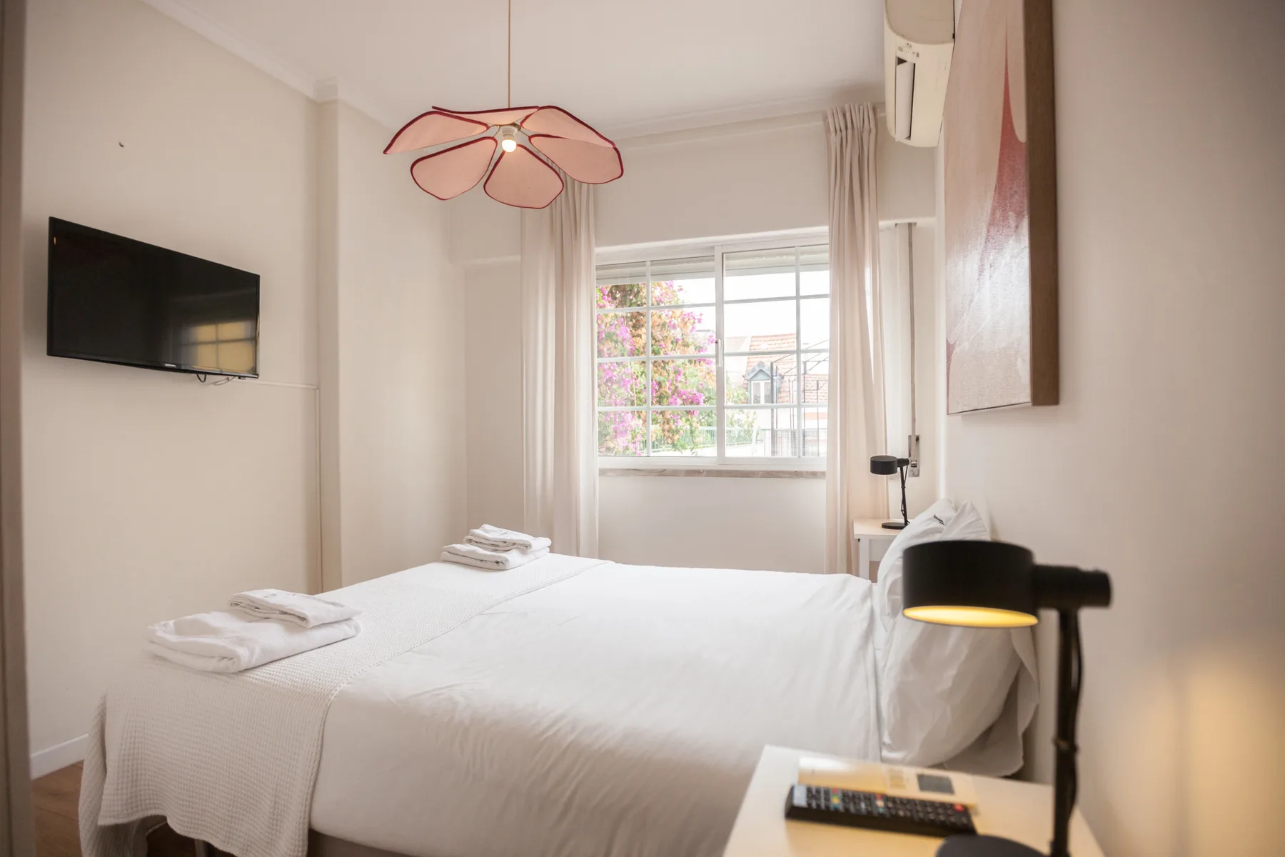 Un dormitorio luminoso con ropa de cama blanca y una ventana con vistas a árboles en flor.