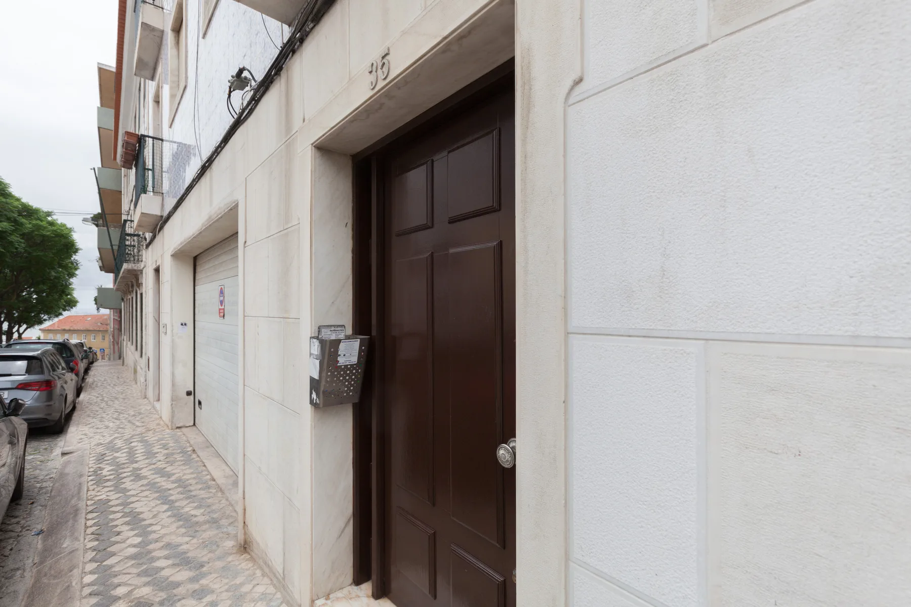 Entrada de un edificio de apartamentos con una puerta de madera oscura junto a una acera embaldosada.