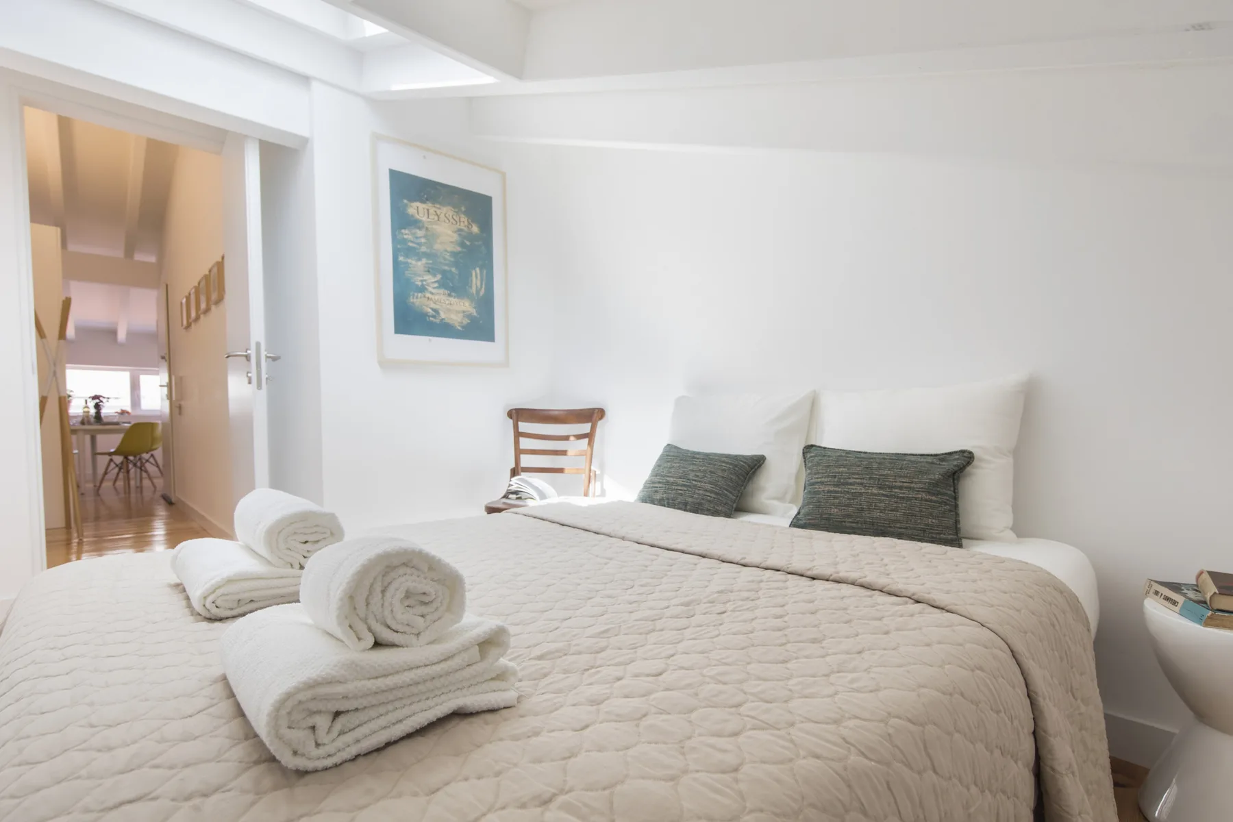 Un dormitorio luminoso con una cama bien tendida y un cuadro en la pared.