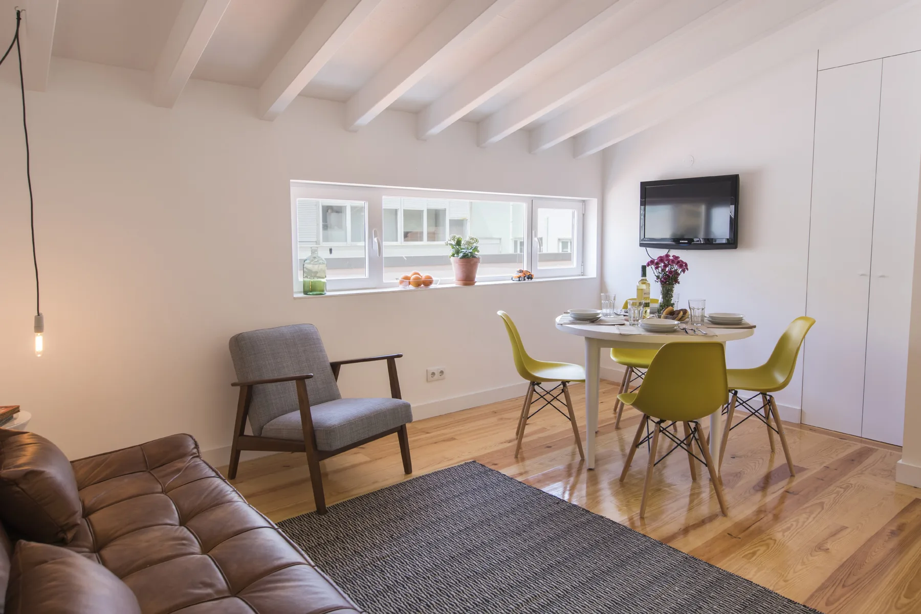 Una zona de estar y comedor con una mesa, sillas y un televisor en la pared.