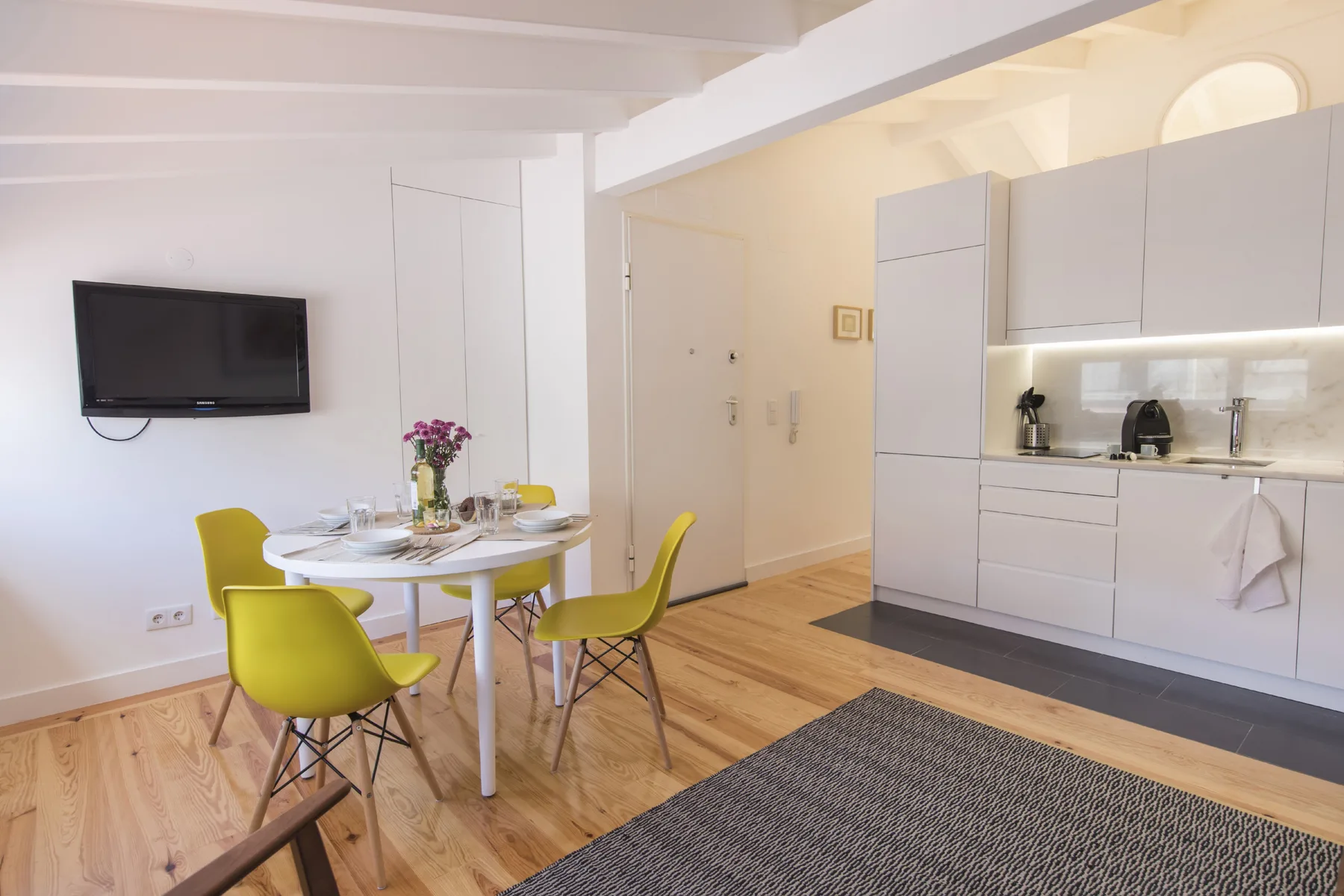 Un comedor con una mesa redonda y asientos verdes junto a una cocina compacta.