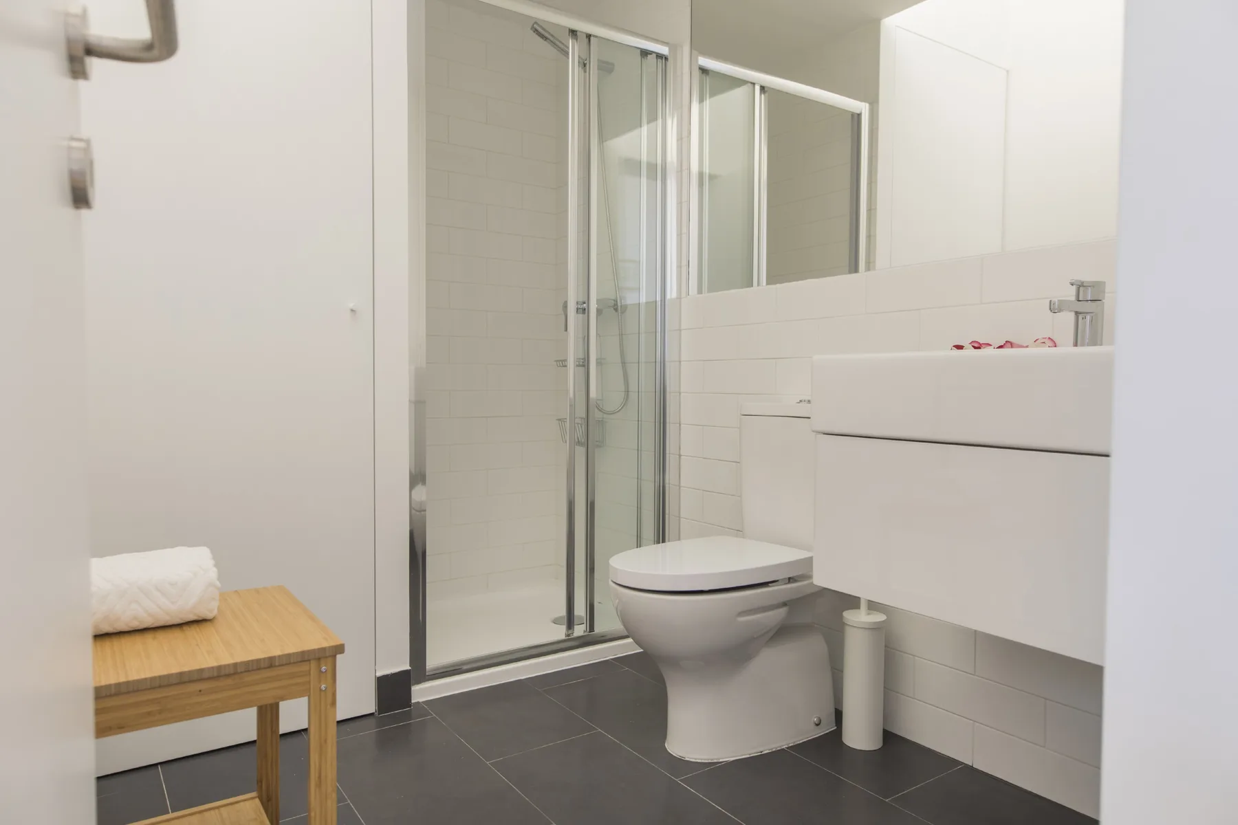 Un baño luminoso con ducha, inodoro y lavabo suspendido.