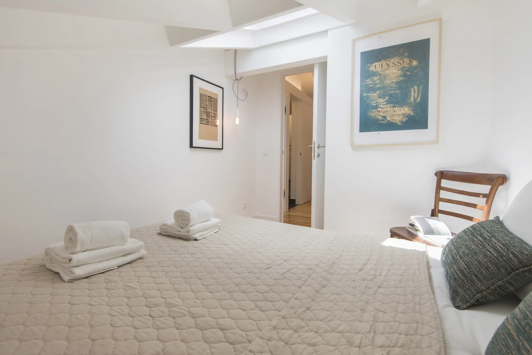 Un dormitorio luminoso con una cama bien tendida y cuadros en las paredes.