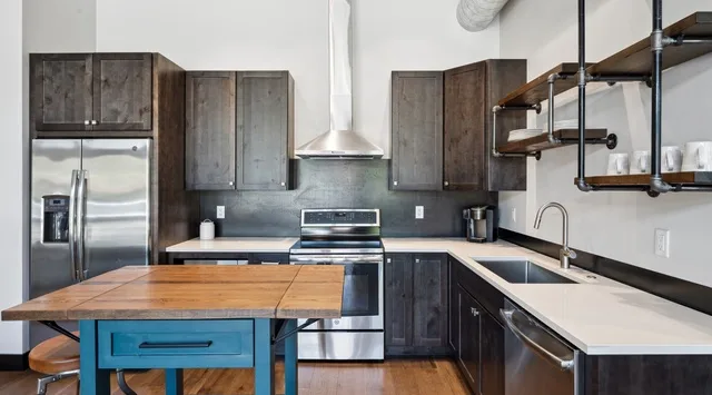 A modern kitchen with dark cabinets, stainless steel appliances, and a wooden island.