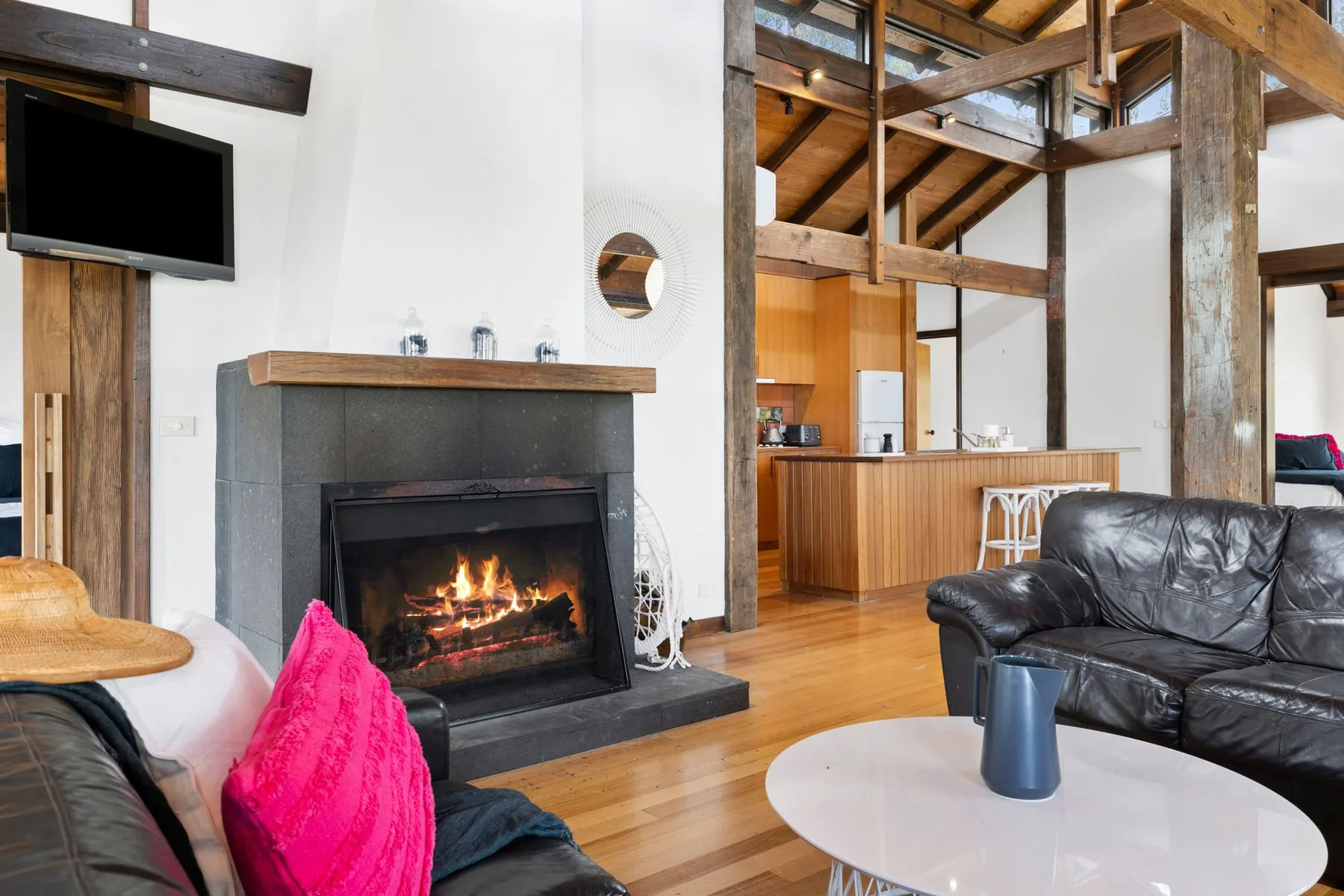 A living room with a fireplace, seating, and exposed wooden beams.