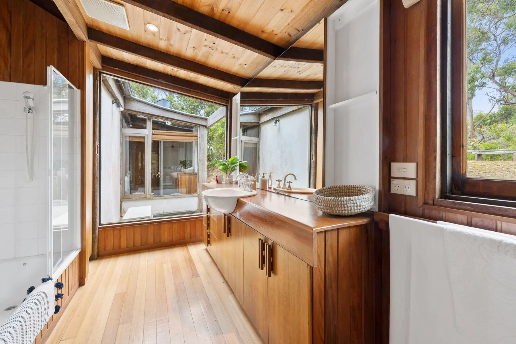 A bright bathroom has a long wooden vanity and large windows.