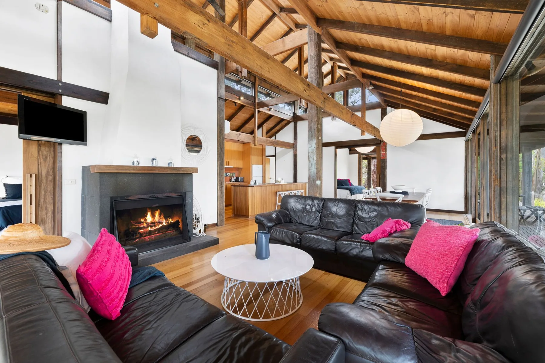 A living room with leather seating, a fireplace, and exposed timber beams.