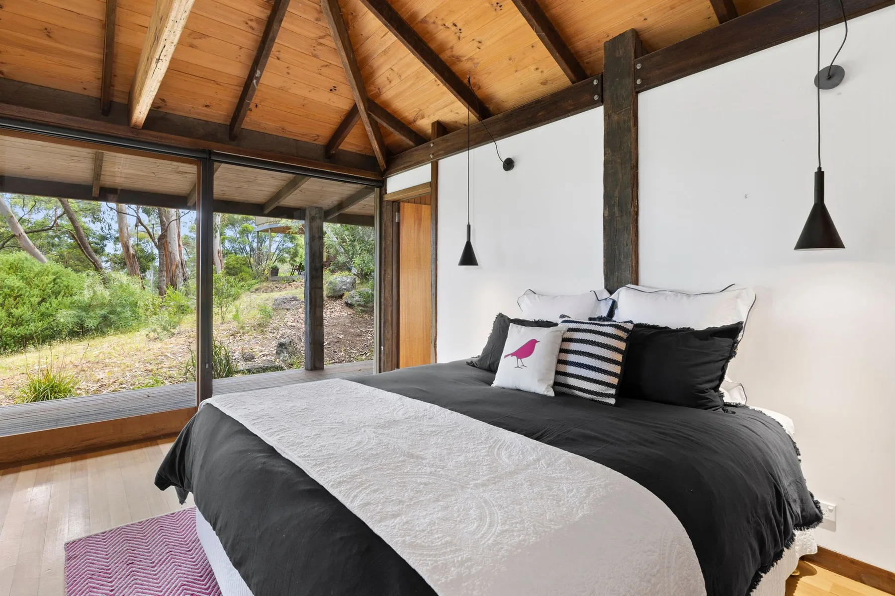 A bedroom with a large bed beside wide windows overlooking greenery.