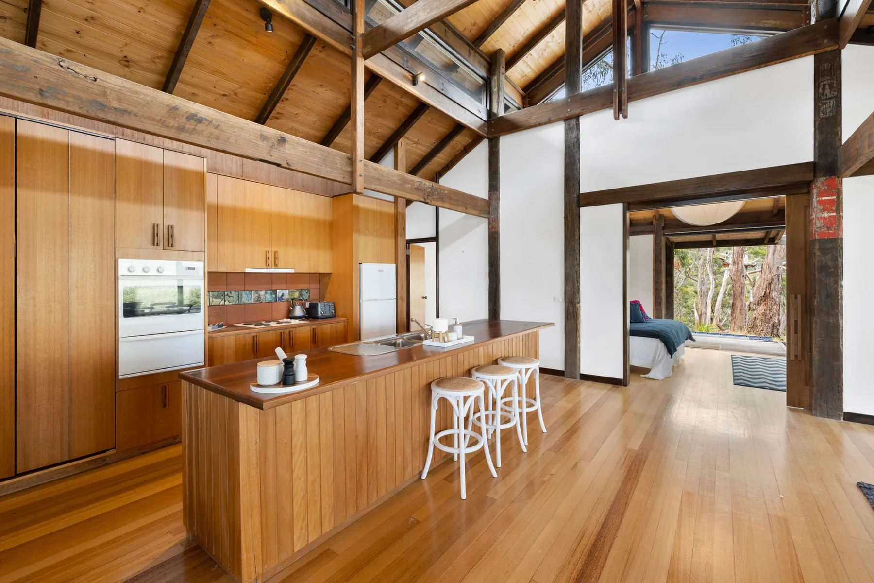 A wood-paneled kitchen with an island and bar seating opens toward a bedroom.