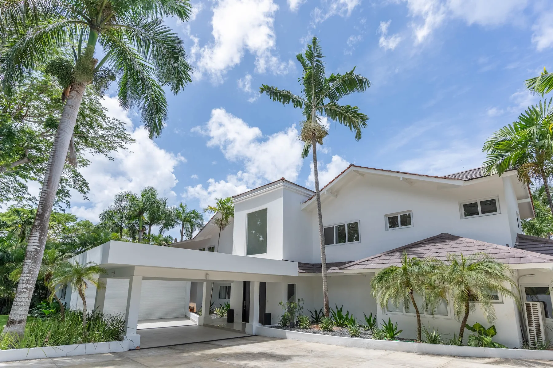 A white modern house stands beneath palm trees and a partly cloudy sky.