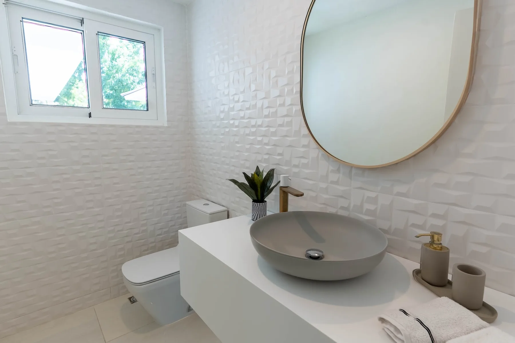 Un tocador de baño con un lavabo redondo sobre encimera queda bajo un espejo grande.