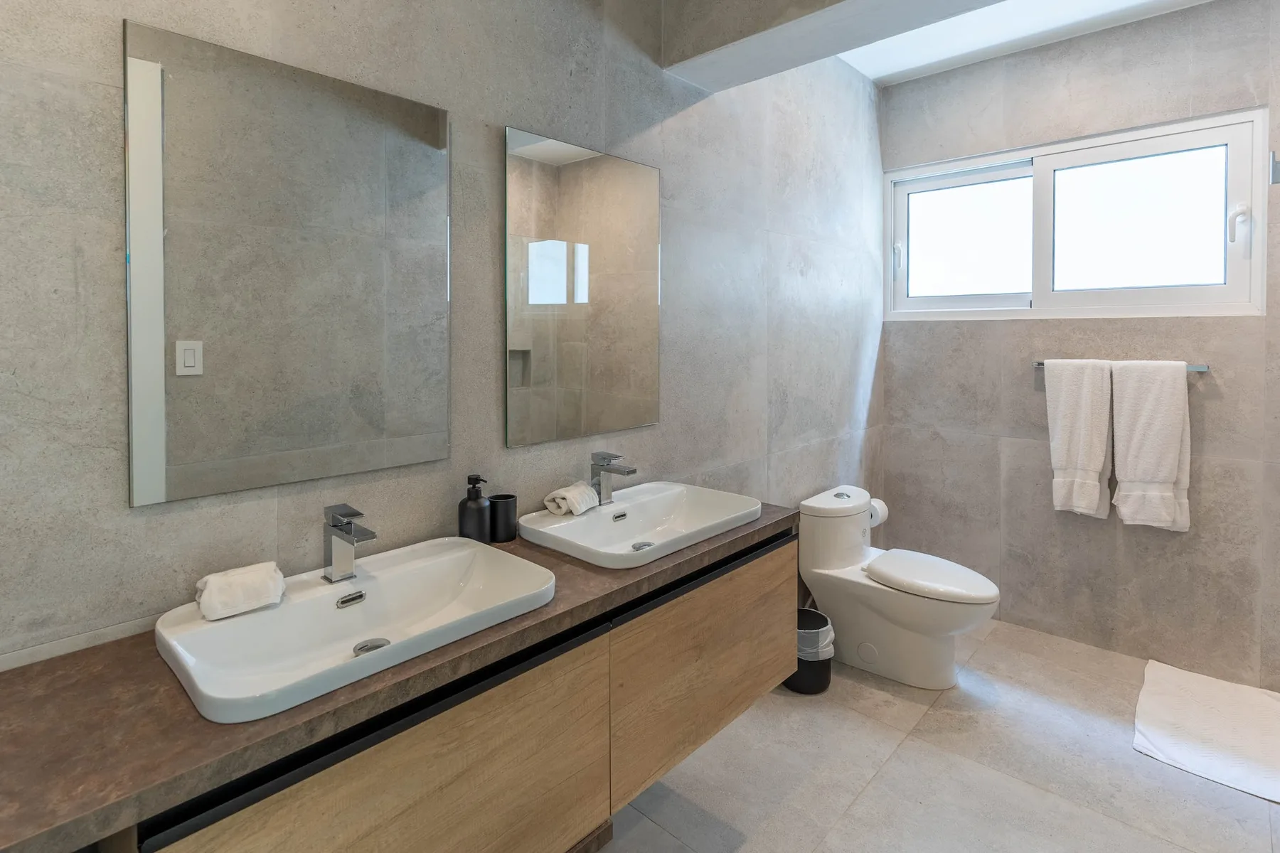 Un baño con dos lavabos, espejos y una ventana sobre el inodoro.