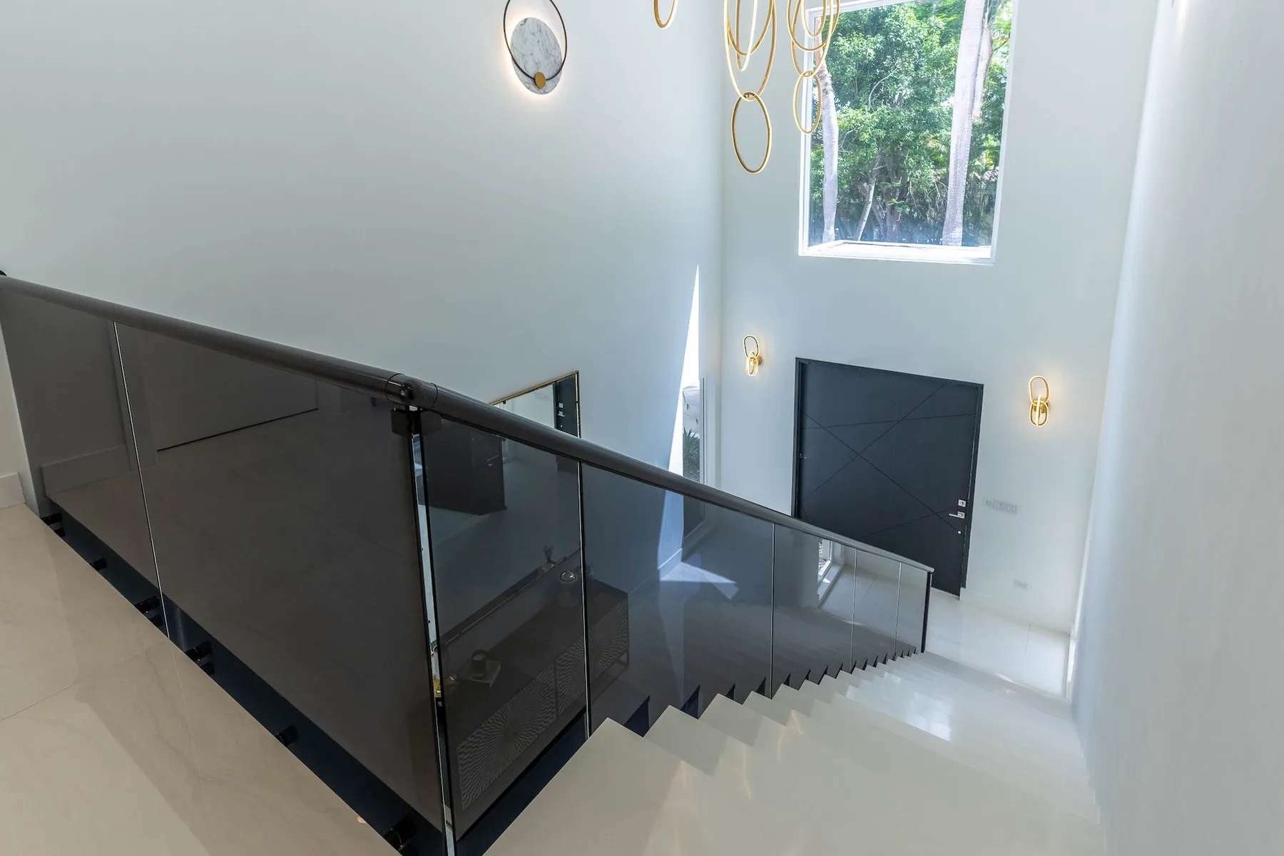 Una escalera interior luminosa con barandillas de vidrio oscuro y una ventana grande.