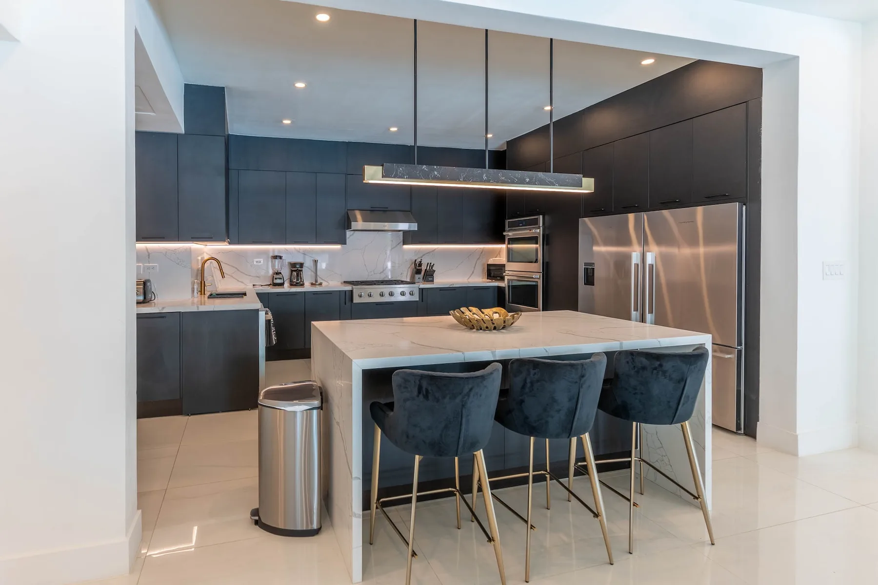 Una cocina moderna con gabinetes oscuros, electrodomésticos de acero inoxidable y una isla con asientos.