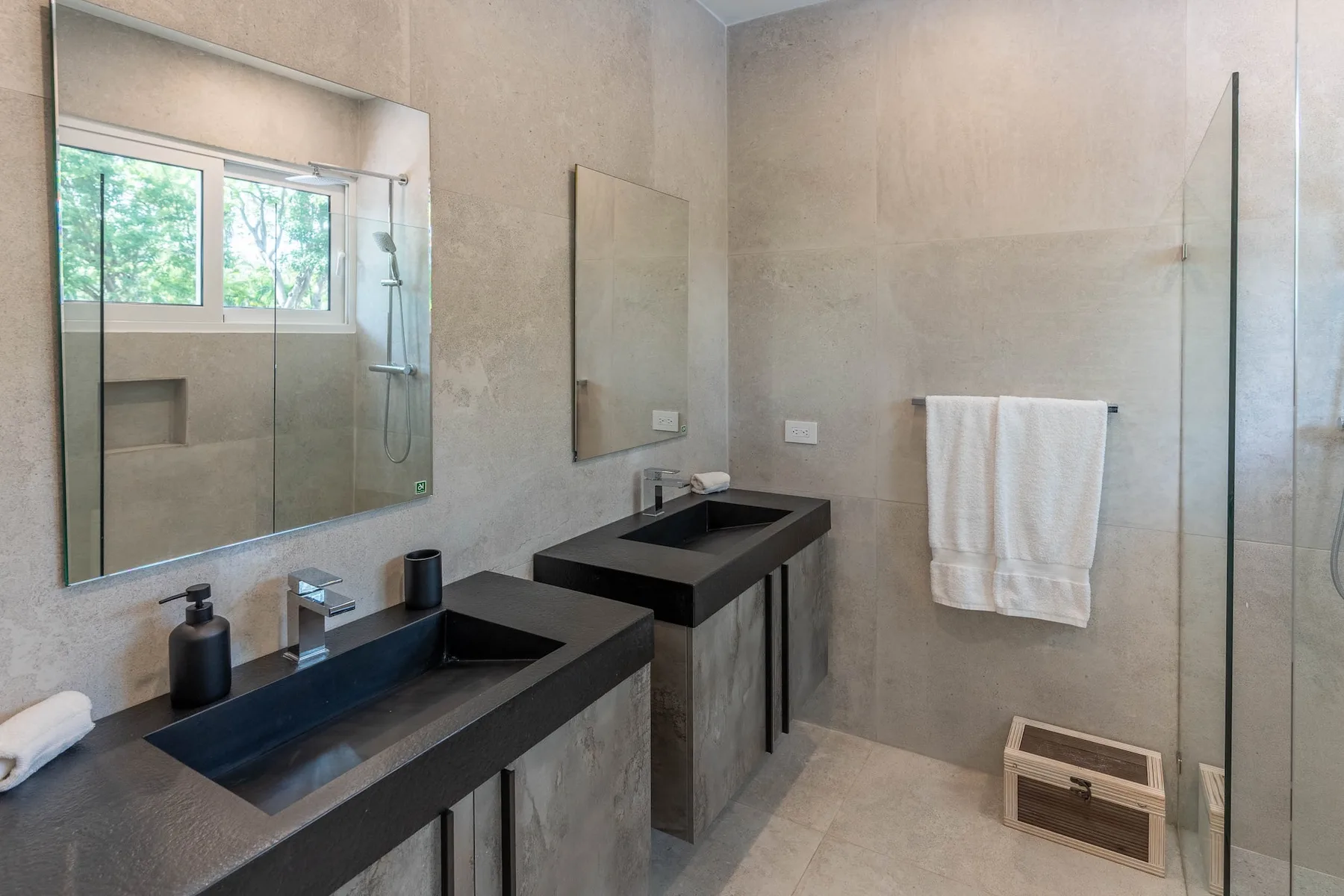 Un baño con dos lavabos oscuros y una ducha de vidrio.