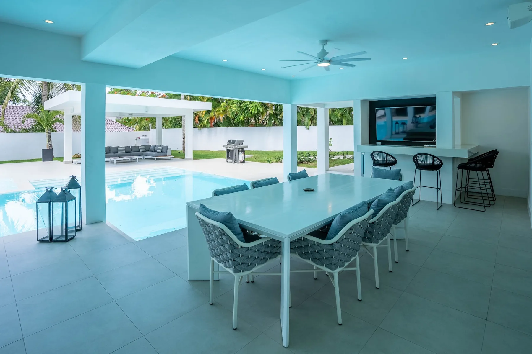 Un comedor cubierto da a una piscina, con una mesa y asientos.