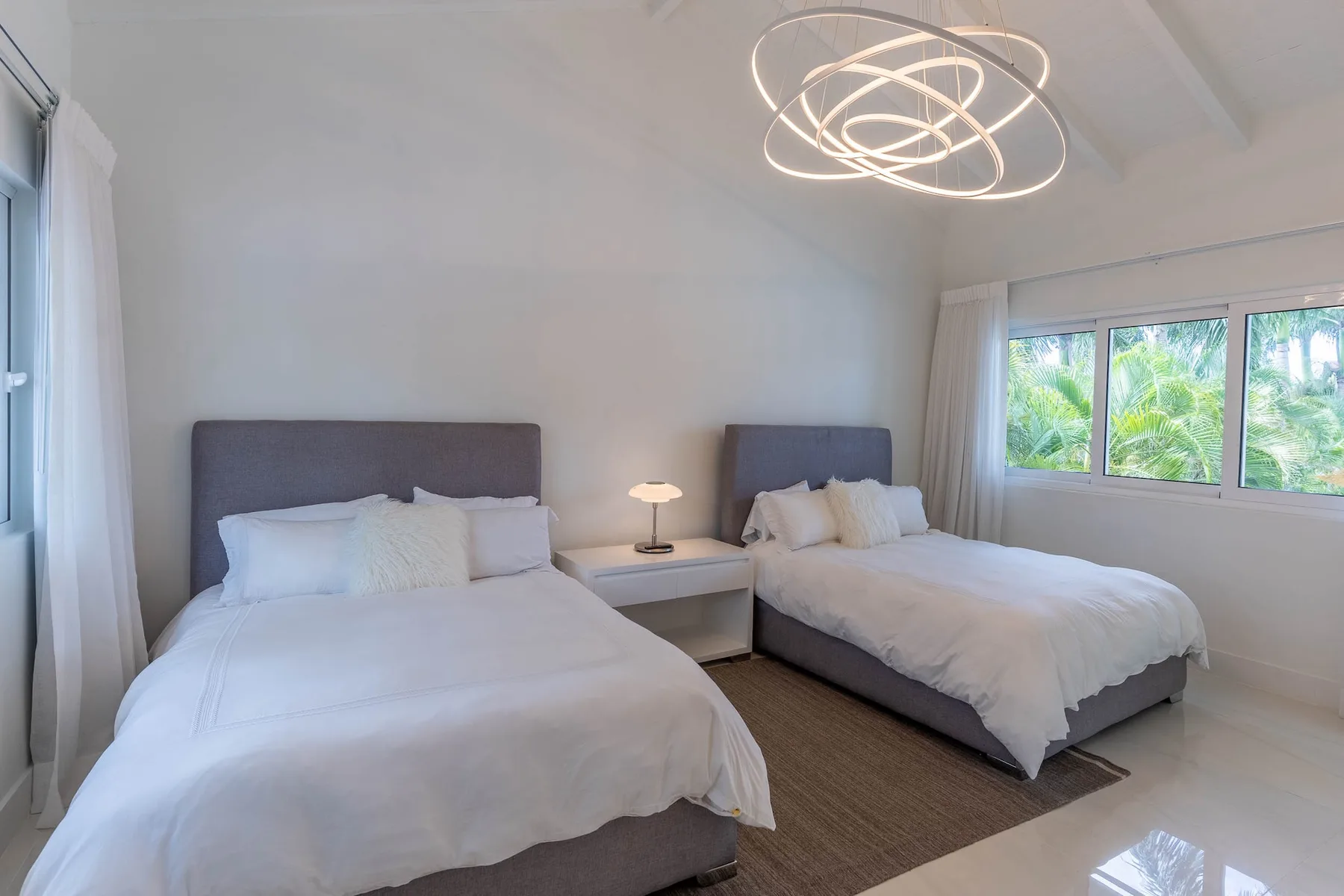 Un dormitorio luminoso con dos camas, una mesa de noche y una ventana grande.
