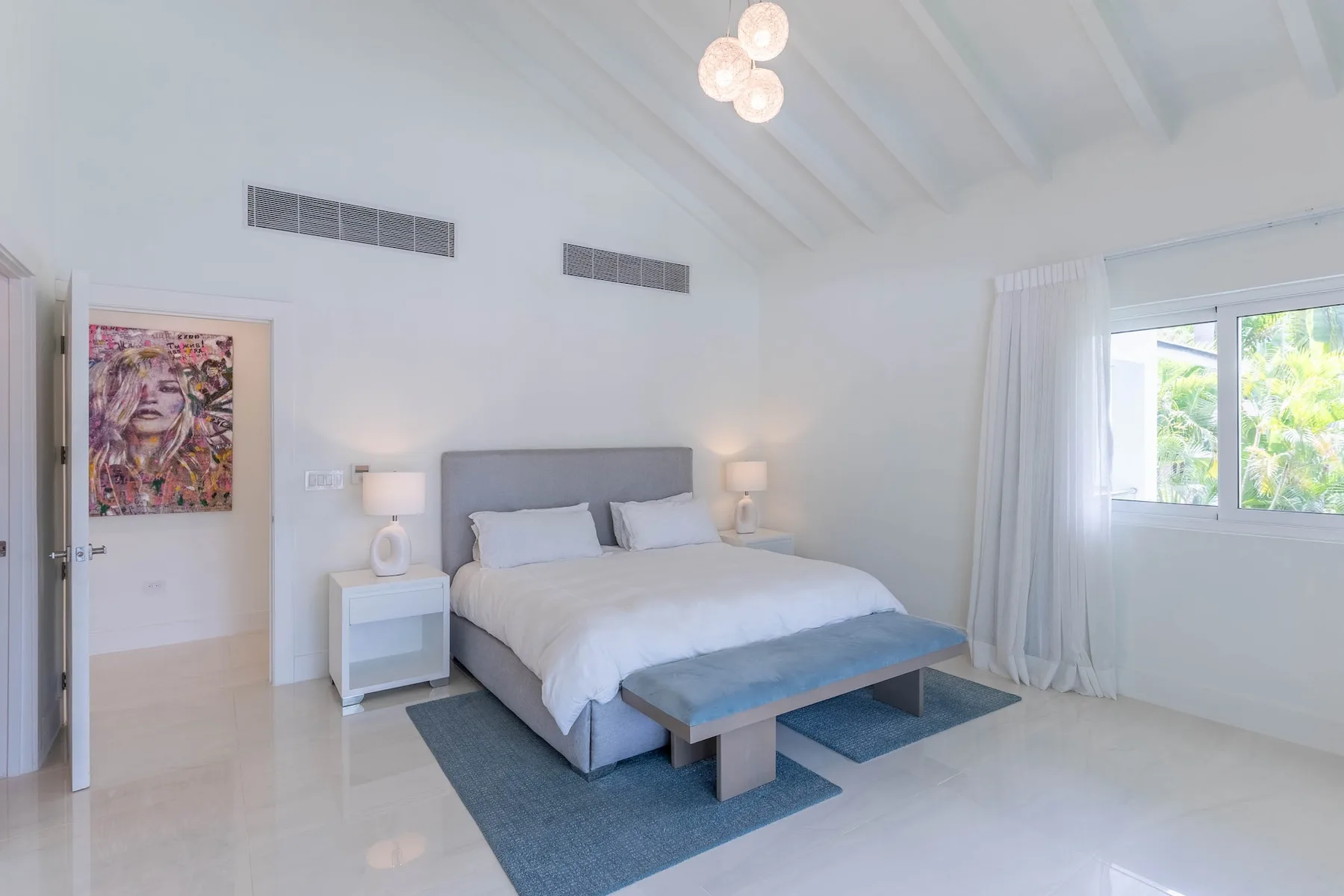 Un dormitorio luminoso con una cama, mesitas de noche y una ventana grande.