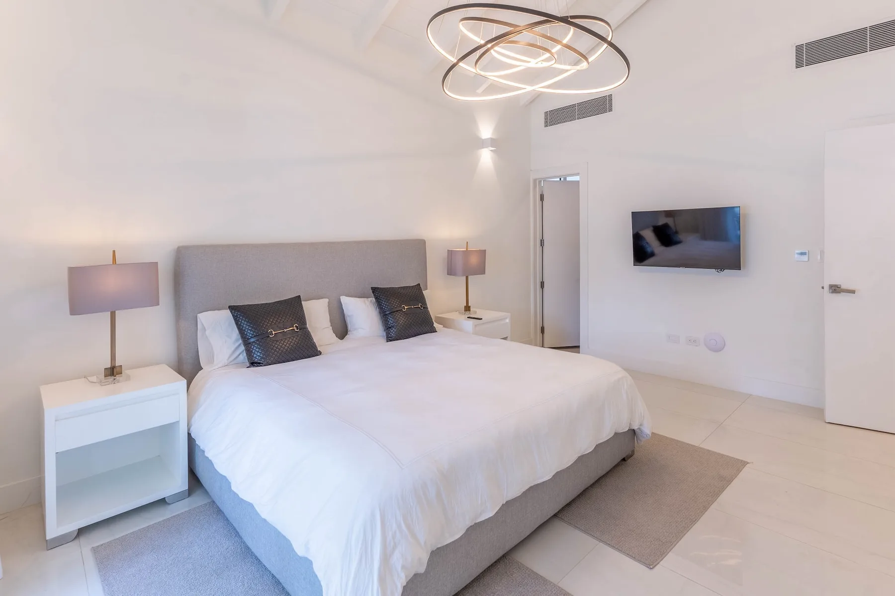 Un dormitorio luminoso con una cama grande y un televisor montado en la pared.