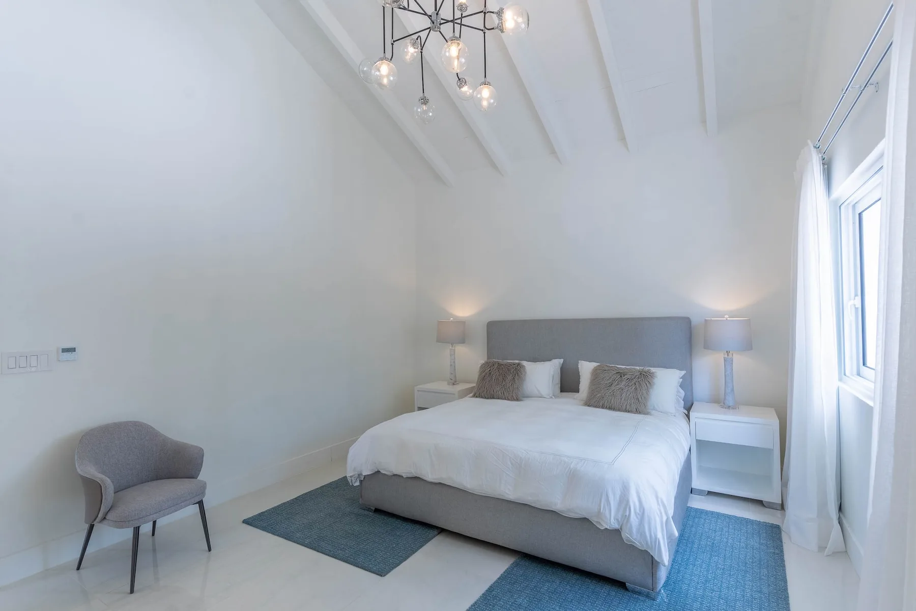 Un dormitorio luminoso con una cama, mesillas de noche y una ventana grande.