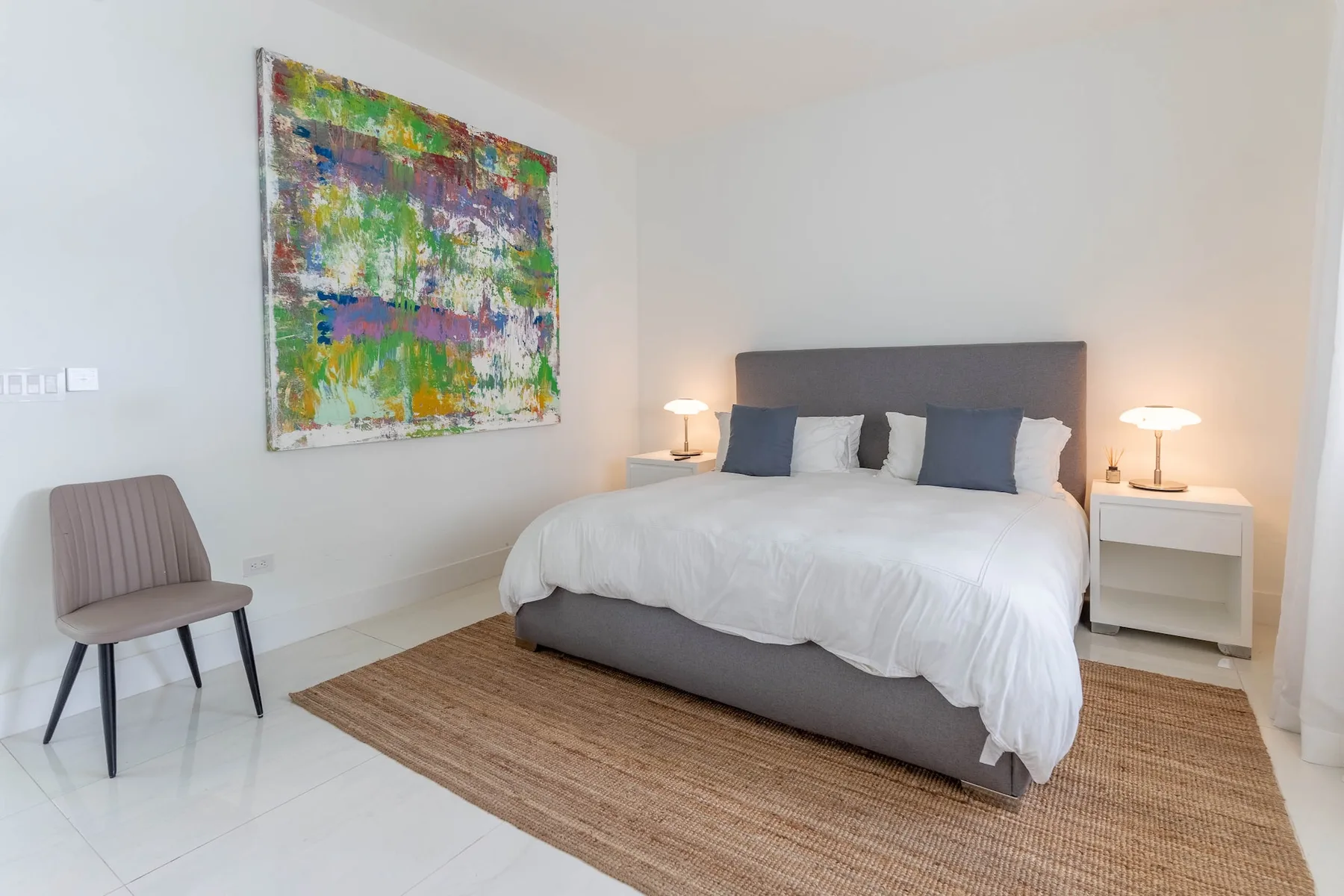 Un dormitorio con una cama, mesitas de noche y arte colorido en la pared.