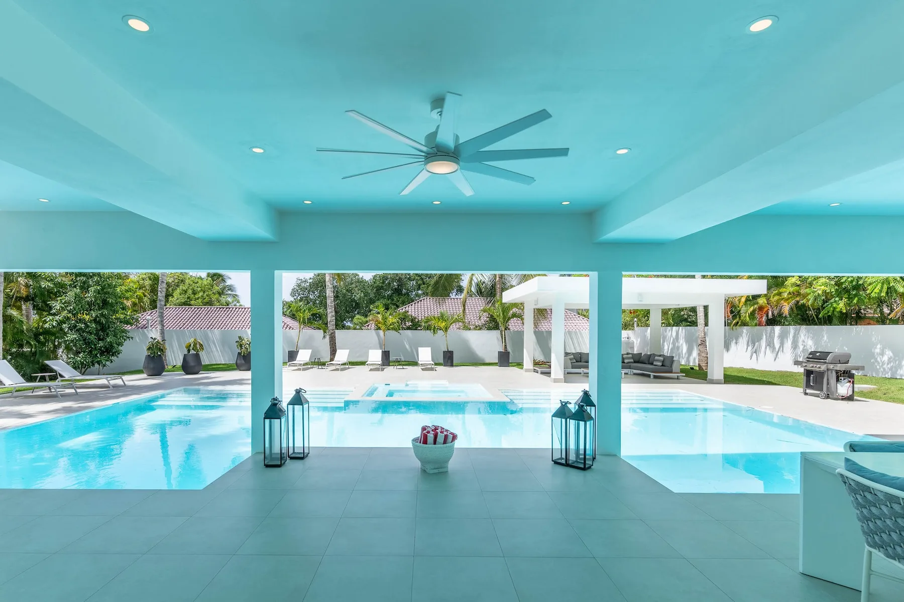 Una zona cubierta junto a la piscina se abre a una piscina y un espacio exterior ajardinado.