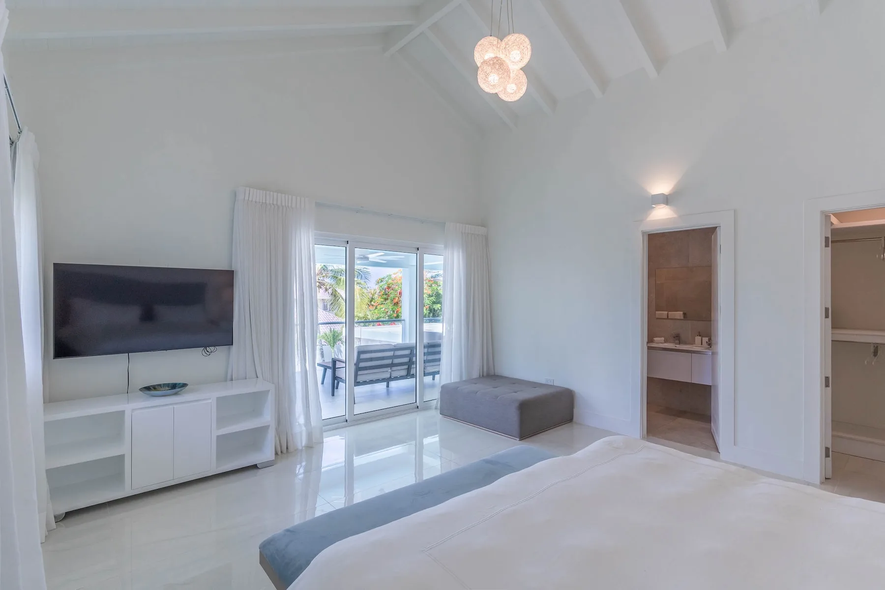 Un dormitorio luminoso con cama, televisor y puertas corredizas de vidrio hacia un patio.