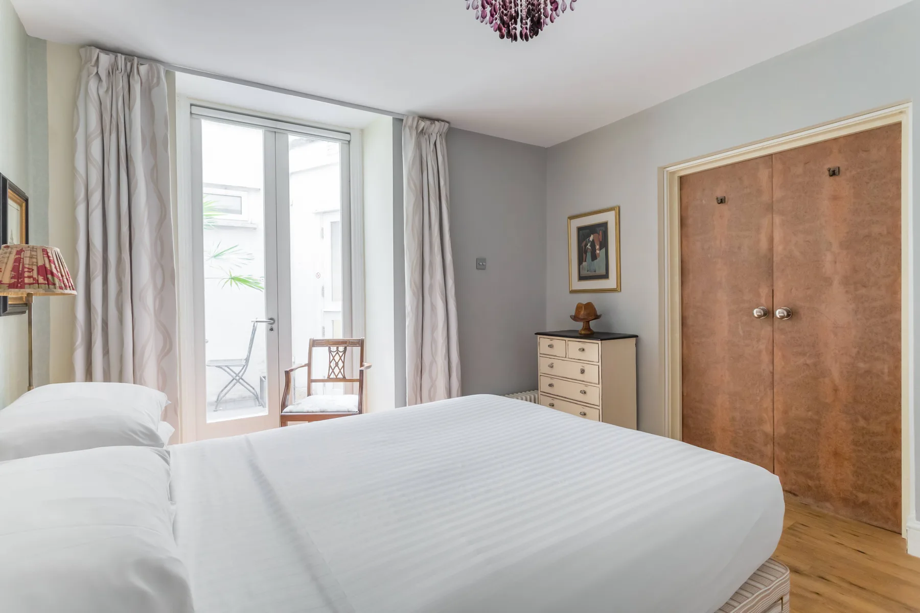 Un dormitorio con una cama bien tendida, una cómoda y una ventana luminosa.