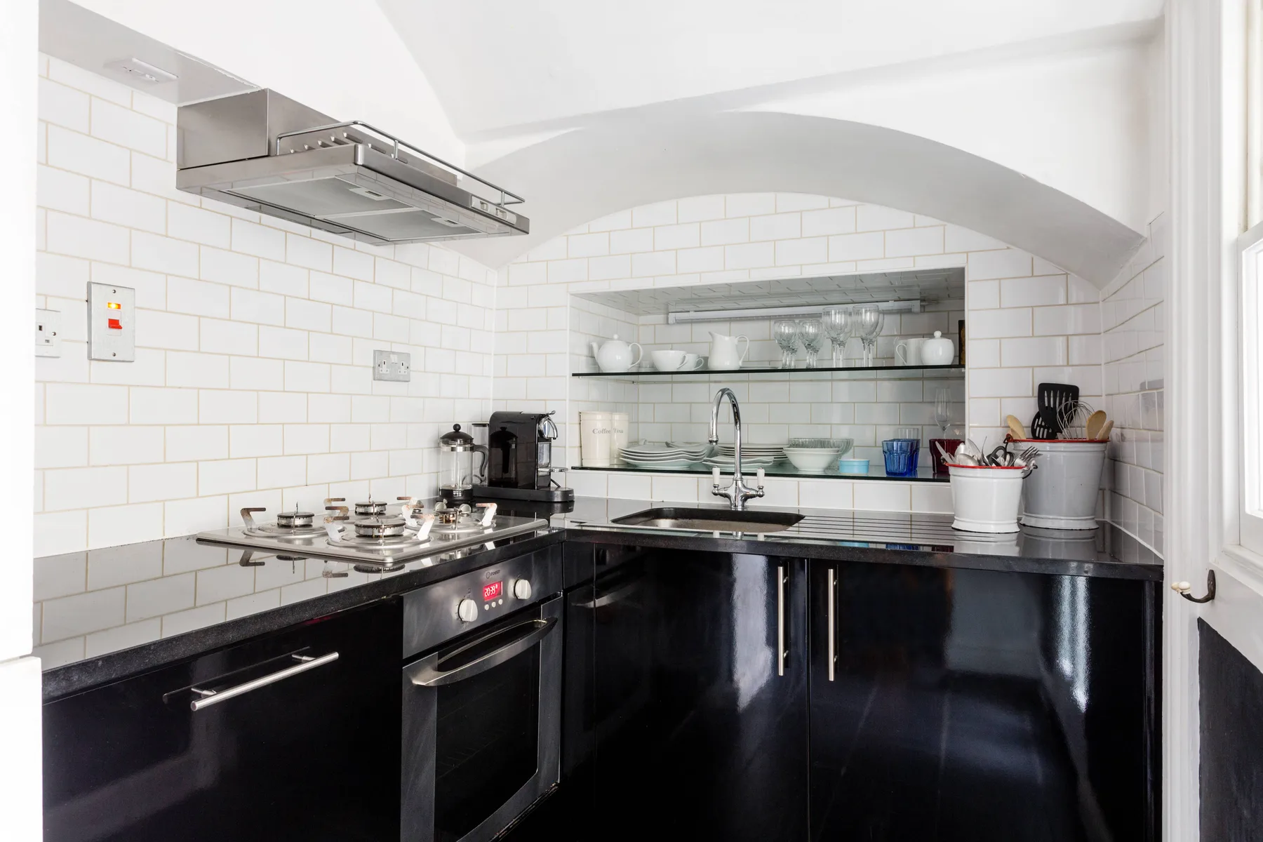 Una cocina luminosa con gabinetes negros, una estufa y un fregadero bajo estantes abiertos.