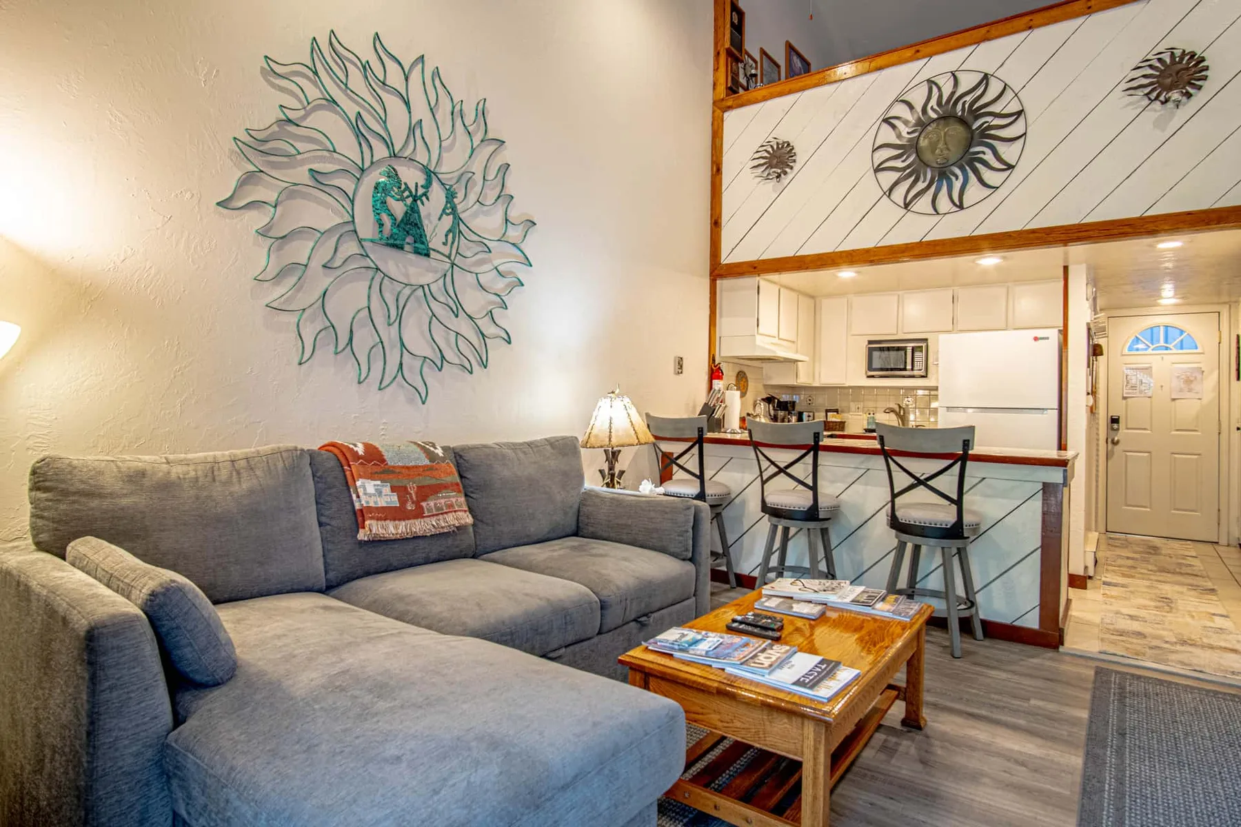Una sala de estar con asientos seccionales y una mesa pequeña da a una cocina abierta.