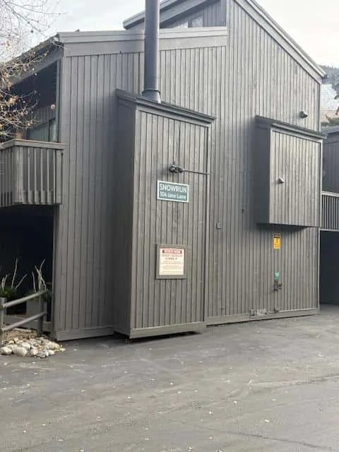 El exterior de un edificio de revestimiento oscuro da a una zona pavimentada, con un tubo de ventilación alto.