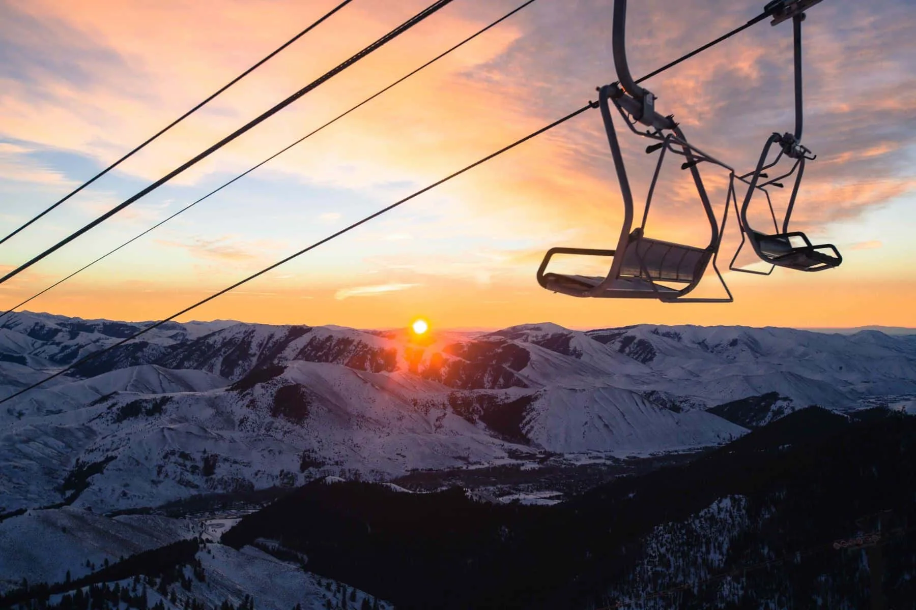 Un telesilla pasa sobre laderas nevadas bajo un cielo colorido al atardecer.