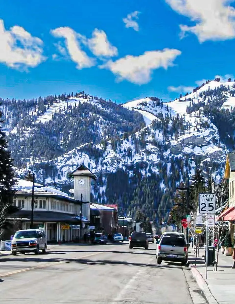 Una calle de montaña se extiende bajo laderas nevadas y un cielo azul brillante.