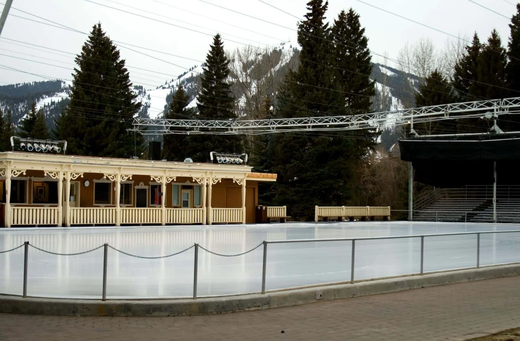 Una pista de hielo al aire libre está junto a un edificio de madera decorado, con árboles de hoja perenne detrás.