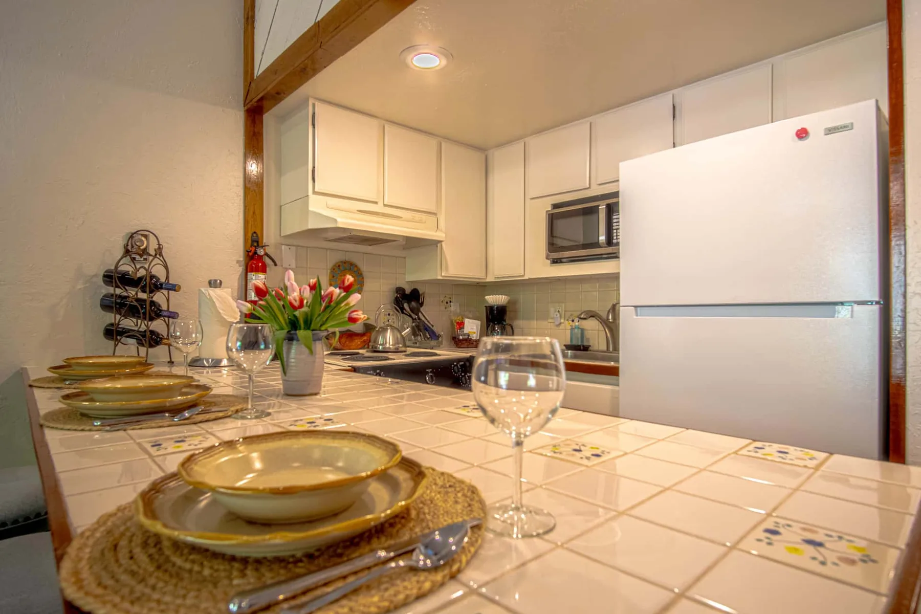 Una encimera de cocina con azulejos está frente a gabinetes blancos, una estufa y un refrigerador.