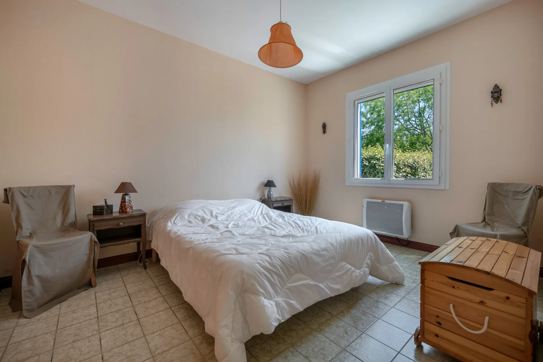 A bedroom with a bed, two chairs, and a window overlooking greenery.