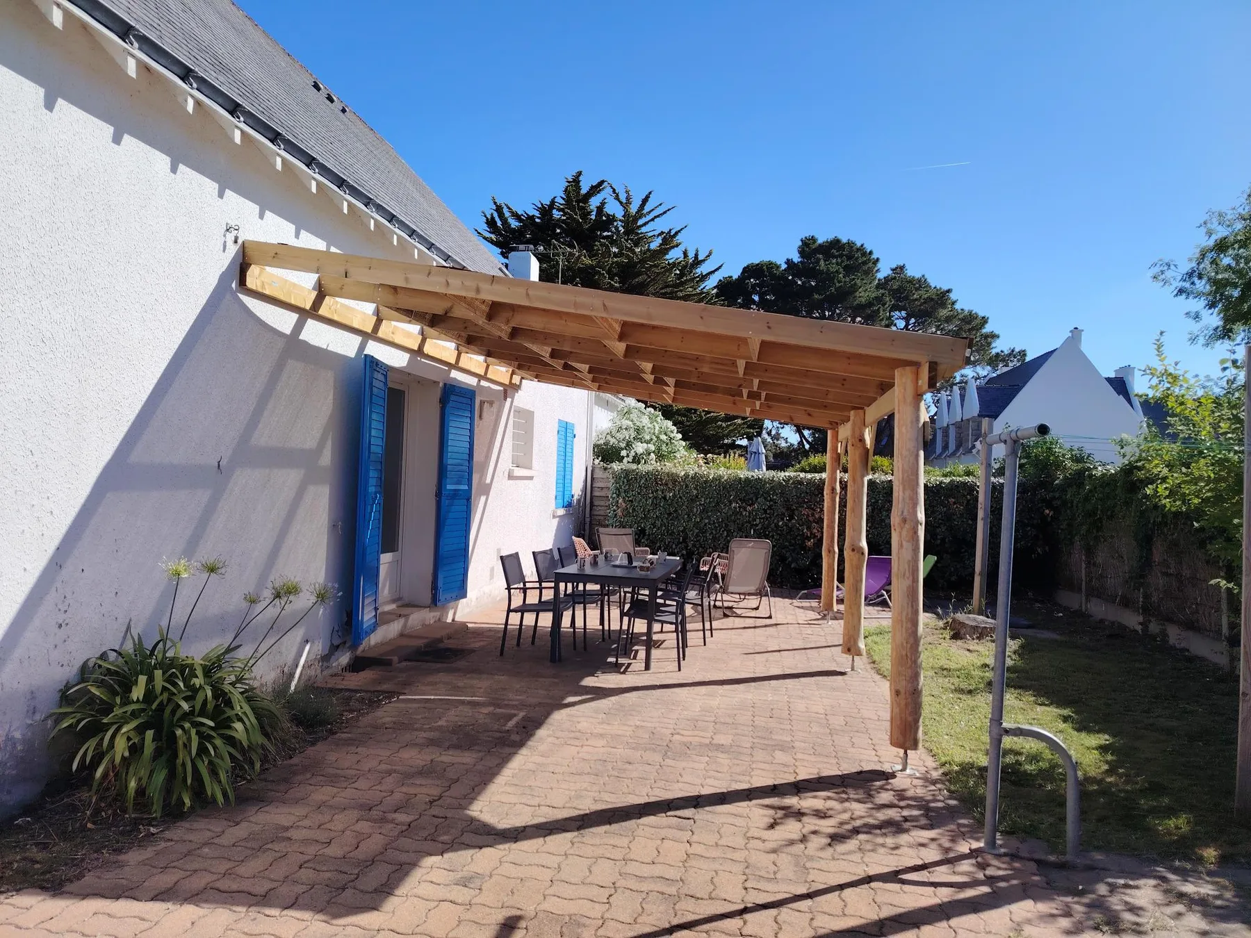 A sunny outdoor patio with a wooden pergola, seating, and a garden.
