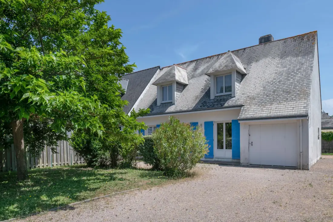A house exterior with a gravel driveway and leafy trees.