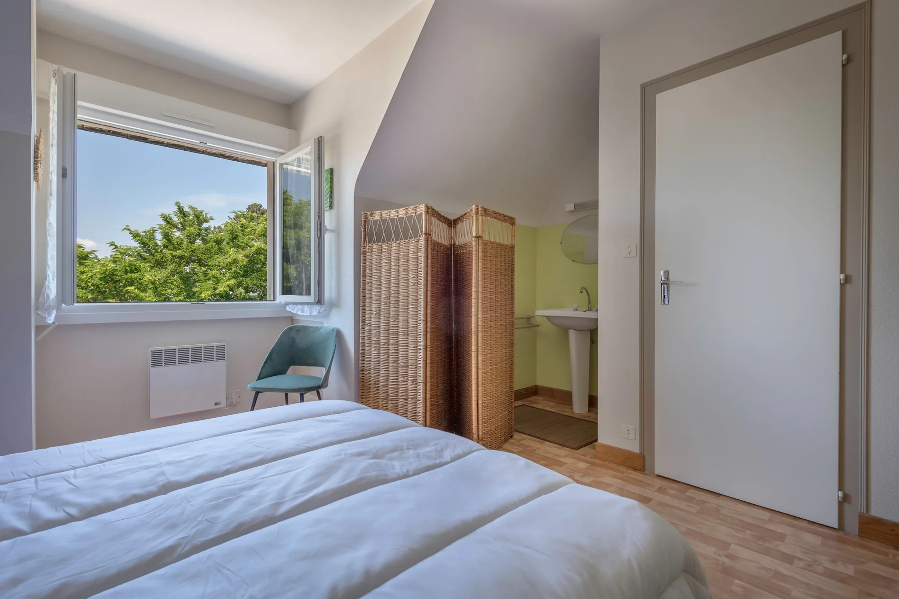 A bedroom with a bed, an open window, and a folding screen.