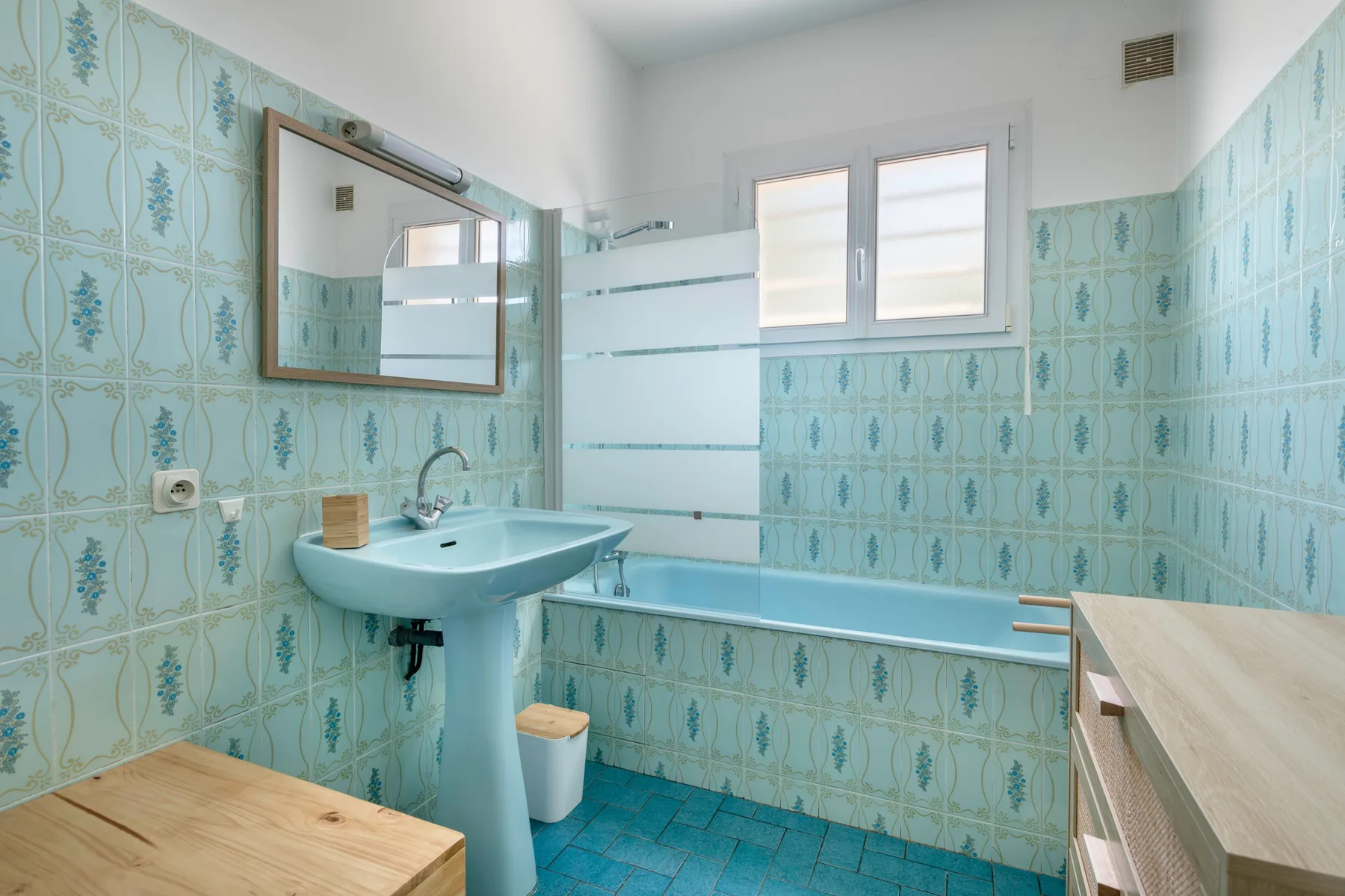A bathroom with a sink, bathtub, and patterned blue wall tiles.