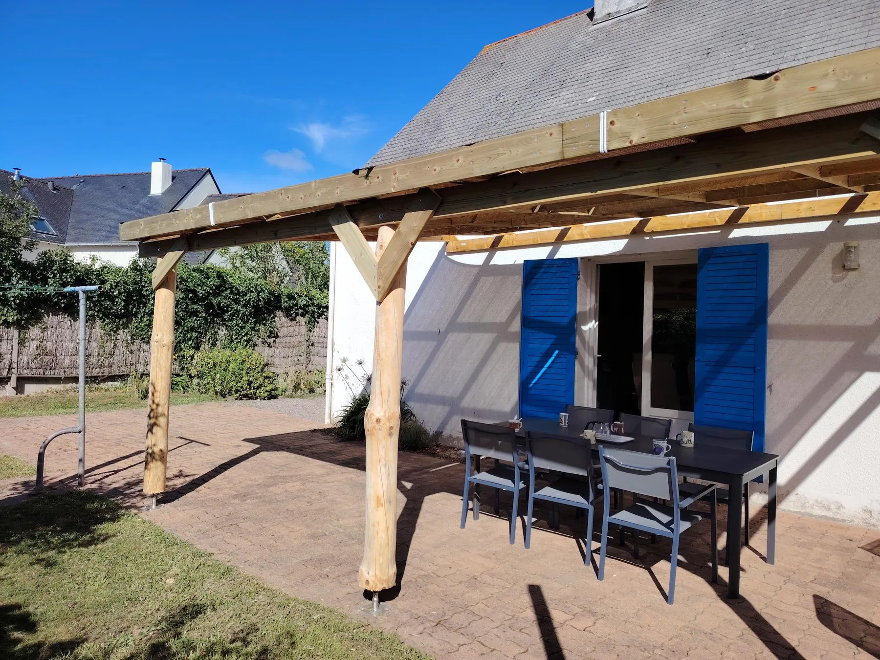 A covered patio with outdoor seating beside a house with blue shutters.