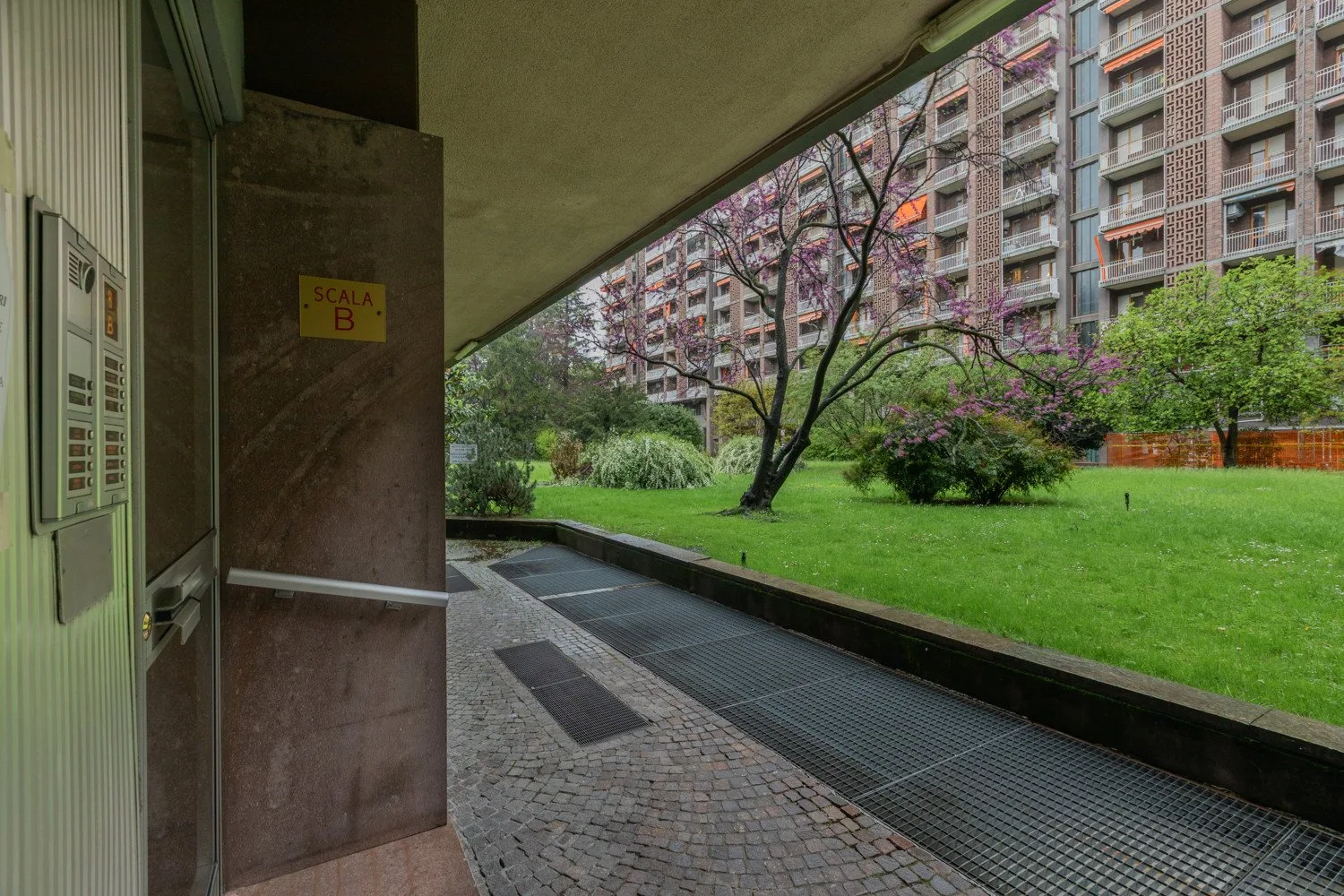 A covered building entrance opens onto a landscaped courtyard with grass and trees.